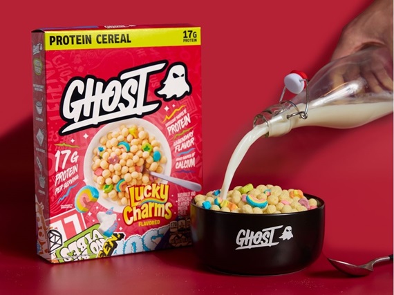 A box of GHOST® PROTEIN CEREAL x LUCKY CHARMS™ next to a bowl labeled “GHOST” with the cereal in it and someone pouring milk into the bowl.
